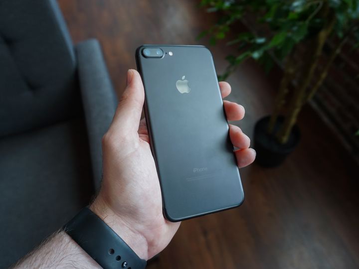 A hand holding a black smartphone outdoors
